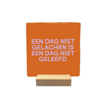 Een dag niet gelachen is een dag niet geleefd - Decoratie tegel - Formaat: - Op deze decoratie tegel staat de tekst "een dag niet gelachen is een dag niet geleefd" in vier regels afgebeeld. De tekst is geschreven in lichtroze letters. De achtergrond van de tegel heeft een oranje kleur. - Snelwenskaart