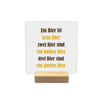 Ein biest ist kein bier - Decoratie tegel - Formaat: - Op deze decoratie tegel staat de tekst "ein bier ist kein bier, zwei bier sind ein halbes bier, drei bier sind ein ganzes bier" in zes regels afgebeeld. De woorden zijn afwisselend in bruine en gele letters geschreven. De achtergrond van de tegel is wit. - Snelwenskaart