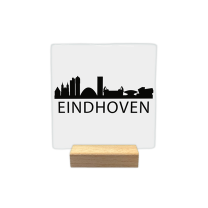 Eindhoven skyline - Decoratie tegel - Formaat: - Op deze decoratie tegel staat een zwarte skyline van Eindhoven afgebeeld tegen een witte achtergrond. Het silhouet toont diverse herkenbare gebouwen uit de stad. Onder de skyline staat in zwarte letters de plaatsnaam Eindhoven. Het gehele ontwerp is uitgevoerd in een minimalistische zwart-witstijl. - Snelwenskaart