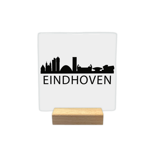 Eindhoven skyline - Decoratie tegel - Formaat: - Op deze decoratie tegel staat een zwarte skyline van Eindhoven afgebeeld tegen een witte achtergrond. Het silhouet toont diverse herkenbare gebouwen uit de stad. Onder de skyline staat in zwarte letters de plaatsnaam Eindhoven. Het gehele ontwerp is uitgevoerd in een minimalistische zwart-witstijl. - Snelwenskaart