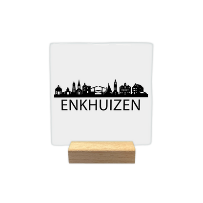 Enkhuizen skyline - Decoratie tegel - Formaat: - Op deze decoratie tegel staat een zwarte skyline van de stad Enkhuizen afgebeeld tegen een witte achtergrond. Het silhouet bevat diverse gebouwen, waaronder een kerk en een ophaalbrug. Onder de skyline staat in zwarte letters de naam Enkhuizen. Het ontwerp is minimalistisch uitgevoerd in alleen zwart en wit. - Snelwenskaart