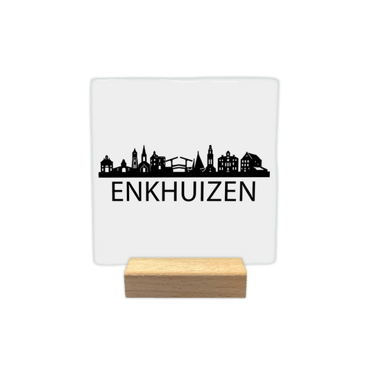 Enkhuizen skyline - Decoratie tegel - Formaat: - Op deze decoratie tegel staat een zwarte skyline van de stad Enkhuizen afgebeeld tegen een witte achtergrond. Het silhouet bevat diverse gebouwen, waaronder een kerk en een ophaalbrug. Onder de skyline staat in zwarte letters de naam Enkhuizen. Het ontwerp is minimalistisch uitgevoerd in alleen zwart en wit. - Snelwenskaart