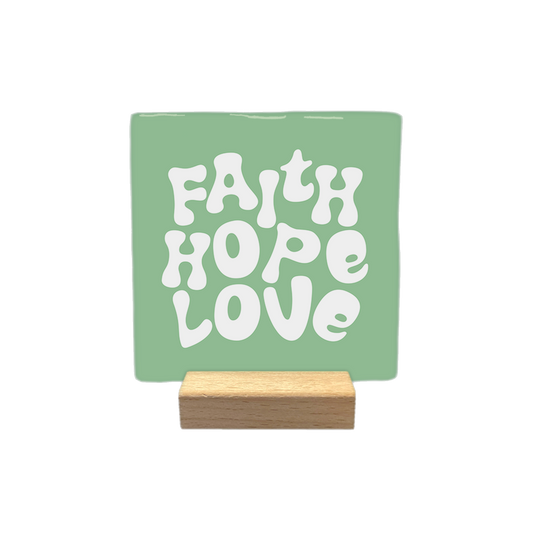 Faith hope love - Decoratie tegel - Formaat: - Op deze decoratietegel staat de tekst "FAITH HOPE LOVE" in witte letters met een speels, golvend lettertype. De tekst is gecentreerd op een groene, vierkante achtergrond. - Snelwenskaart