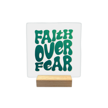 Faith over fear - Decoratie tegel - Formaat: - Op deze decoratie tegel staat de tekst "Faith over fear" in grote, speelse letters. De letters hebben een groene kleur met een verloop van donker naar licht. De tekst is centraal op een witte achtergrond geplaatst. - Snelwenskaart