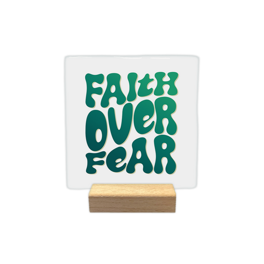 Faith over fear - Decoratie tegel - Formaat: - Op deze decoratie tegel staat de tekst "Faith over fear" in grote, speelse letters. De letters hebben een groene kleur met een verloop van donker naar licht. De tekst is centraal op een witte achtergrond geplaatst. - Snelwenskaart