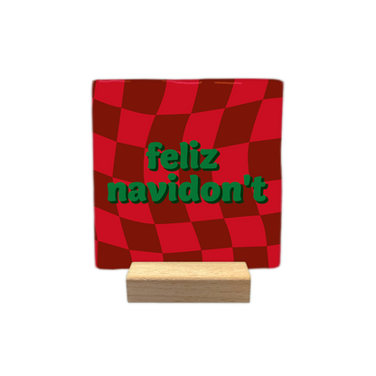 Feliz navidon't - Decoratie tegel - Formaat: - Op deze decoratie tegel staat een rood met donkerrood geblokt patroon dat een golvend effect heeft. In het midden staat de tekst feliz navidon't in groene letters gedrukt. - Snelwenskaart