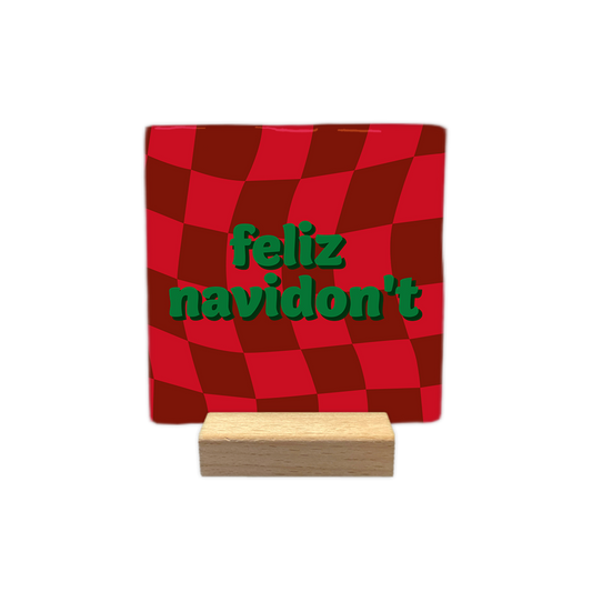 Feliz navidon't - Decoratie tegel - Formaat: - Op deze decoratie tegel staat een rood met donkerrood geblokt patroon dat een golvend effect heeft. In het midden staat de tekst feliz navidon't in groene letters gedrukt. - Snelwenskaart