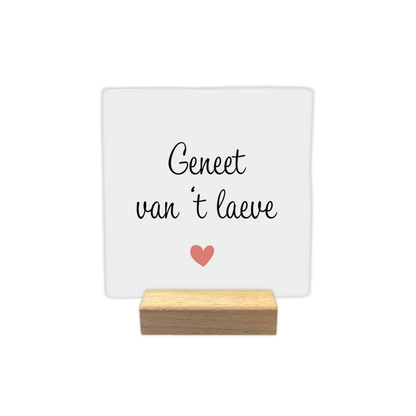 Geneet van 't laeve - Decoratie tegel - Formaat: - Op deze decoratie tegel staat de tekst "Geneet van 't laeve" in zwarte letters. De tekst is verdeeld over twee regels op een witte achtergrond. Onder de tekst staat een klein, roze hartje. Het gebruikte lettertype is cursief en sierlijk. - Snelwenskaart
