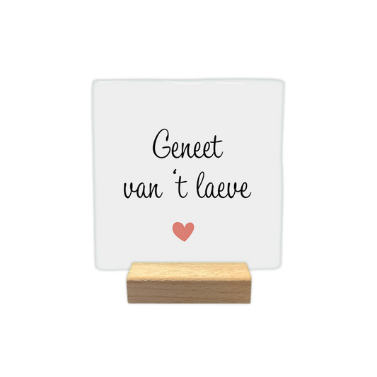 Geneet van 't laeve - Decoratie tegel - Formaat: - Op deze decoratie tegel staat de tekst "Geneet van 't laeve" in zwarte letters. De tekst is verdeeld over twee regels op een witte achtergrond. Onder de tekst staat een klein, roze hartje. Het gebruikte lettertype is cursief en sierlijk. - Snelwenskaart