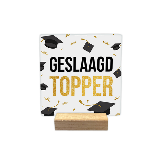 Geslaagd topper - Decoratie tegel - Formaat: - Op deze decoratie tegel staan meerdere afstudeerhoeden. In het midden van de tegel staat in het zwart de tekst 'geslaagd' en daaronder in het geel de tekst 'topper'. - Snelwenskaart