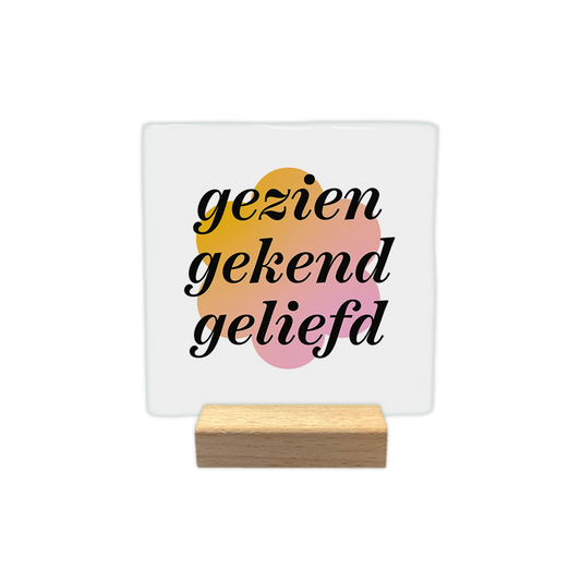 Gezien gekend geliefd - Decoratie tegel - Formaat: - Op deze decoratie tegel staat de tekst "gezien gekend geliefd" in zwarte, schuingedrukte letters. De tekst is geplaatst over een abstracte, bloemvormige achtergrond in tinten van geel naar roze. Het geheel is gecentreerd op een witte ondergrond. - Snelwenskaart