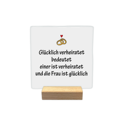 Glücklich verheiratet - Decoratie tegel - Formaat: - Op deze decoratie tegel staat de tekst "glücklich verheiratet bedeutet einer ist verheiratet und die frau ist glücklich" in zwarte letters afgebeeld. Boven de tekst staan twee in elkaar grijpende trouwringen met een klein rood hartje erboven. De achtergrond van de tegel is wit. - Snelwenskaart