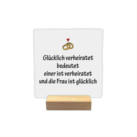 Glücklich verheiratet - Decoratie tegel - Formaat: - Op deze decoratie tegel staat de tekst "glücklich verheiratet bedeutet einer ist verheiratet und die frau ist glücklich" in zwarte letters afgebeeld. Boven de tekst staan twee in elkaar grijpende trouwringen met een klein rood hartje erboven. De achtergrond van de tegel is wit. - Snelwenskaart