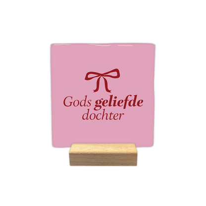 Gods geliefde dochter - Decoratie tegel - Formaat: - Op deze decoratie tegel staat bovenaan een rode strik afgebeeld. Daaronder staat de tekst "Gods geliefde dochter" in rode letters. Het geheel is geplaatst tegen een lichtroze achtergrond. - Snelwenskaart