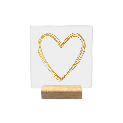 Gouden hart - Decoratie tegel - Formaat: - Op deze decoratietegel staat centraal een hartvorm afgebeeld die is getekend met meerdere overlappende lijnen in een goudkleurige textuur. De achtergrond van de illustratie is effen wit. Er is geen verdere tekst op de afbeelding aanwezig. - Snelwenskaart