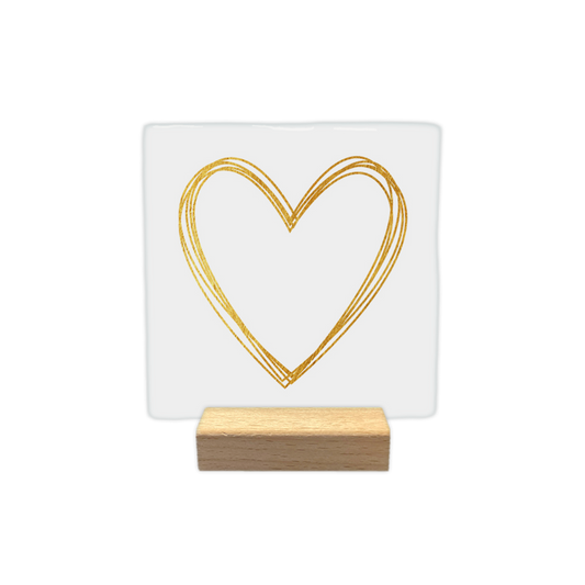 Gouden hart - Decoratie tegel - Formaat: - Op deze decoratietegel staat centraal een hartvorm afgebeeld die is getekend met meerdere overlappende lijnen in een goudkleurige textuur. De achtergrond van de illustratie is effen wit. Er is geen verdere tekst op de afbeelding aanwezig. - Snelwenskaart