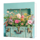 Koffer vol bloemen - Formaat: Standaard - Vorm: Vierkant - Blanco kaart - Op deze wenskaart staat een illustratie van een oude, lichtblauwe koffer die tot de rand toe gevuld is met een kleurrijke mix van diverse veldbloemen en zomerbloemen in zachte tinten zoals roze, geel en wit. De koffer heeft een vintage uitstraling met messingkleurige details en slijtageplekken, en staat afgebeeld tegen een effen lichtblauwe achtergrond. Er is geen tekst op de illustratie zichtbaar. - Snelwenskaart