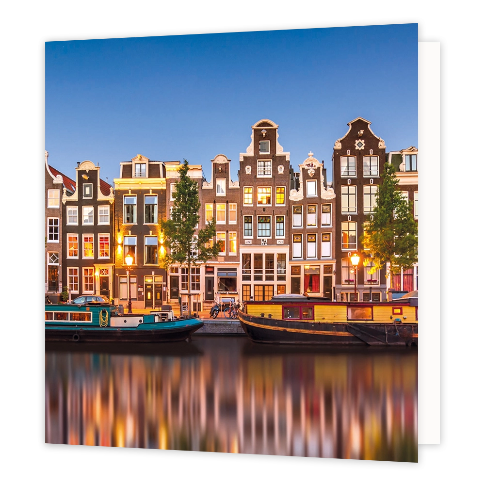 Amsterdamse grachten - Formaat: Standaard - Vorm: Vierkant - Blanco kaart - Op deze wenskaart staat een illustratie van historische Amsterdamse grachtenpanden tijdens de schemering, met sfeervol verlichte ramen en straatlantaarns. Langs de kade en in het water liggen woonboten, en de lichten van de stad weerspiegelen prachtig in het water. De hemel erboven is helderblauw en er is geen tekst op de illustratie zichtbaar. - Snelwenskaart