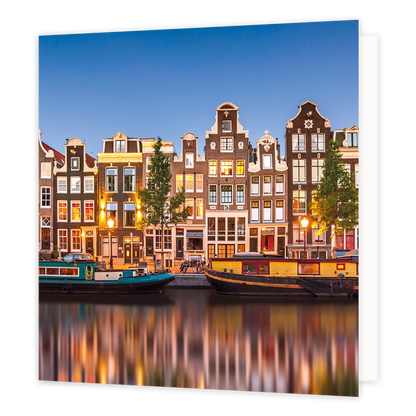 Amsterdamse grachten - Formaat: Standaard - Vorm: Vierkant - Blanco kaart - Op deze wenskaart staat een illustratie van historische Amsterdamse grachtenpanden tijdens de schemering, met sfeervol verlichte ramen en straatlantaarns. Langs de kade en in het water liggen woonboten, en de lichten van de stad weerspiegelen prachtig in het water. De hemel erboven is helderblauw en er is geen tekst op de illustratie zichtbaar. - Snelwenskaart