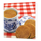 Stroopwafels - Formaat: Standaard - Vorm: Vierkant - Blanco kaart - Op deze wenskaart staat een illustratie van een traditionele blauw-witte Delfts blauwe voorraadpot gevuld met stroopwafels, geplaatst op een rood-wit geruite tafel. Naast de pot ligt het bijbehorende deksel met een bloemmotief en zijn er nog drie stroopwafels voor de pot neergelegd. Er is geen tekst op de illustratie zichtbaar. - Snelwenskaart