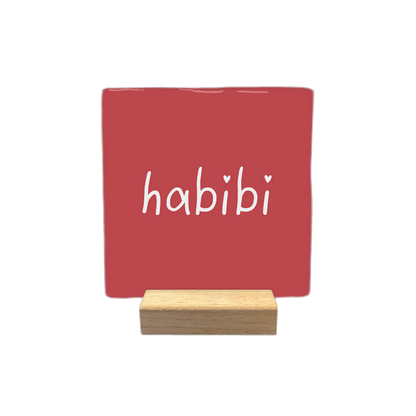 Habibi - Decoratie tegel - Formaat: - Op deze decoratietegel staat het woord "habibi" in witte, handgeschreven letters. De twee puntjes op de "i"-letters zijn vervangen door kleine witte hartjes. De tekst is gecentreerd op een roze-rode achtergrond. - Snelwenskaart