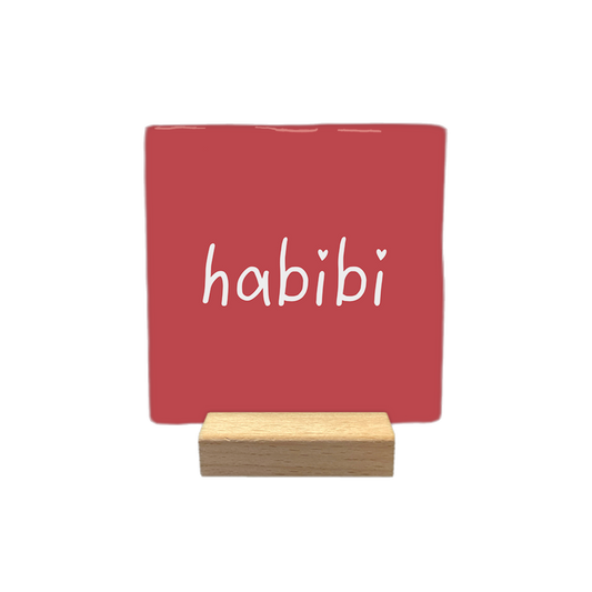 Habibi - Decoratie tegel - Formaat: - Op deze decoratietegel staat het woord "habibi" in witte, handgeschreven letters. De twee puntjes op de "i"-letters zijn vervangen door kleine witte hartjes. De tekst is gecentreerd op een roze-rode achtergrond. - Snelwenskaart