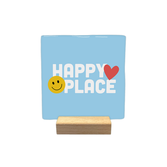 Happy place - Decoratie tegel - Formaat: - Op deze decoratietegel staat in het midden de tekst "HAPPY PLACE" in witte hoofdletters met een afgerond lettertype. Aan de linkerzijde van het woord "HAPPY" is een geel smiley-icoontje geplaatst, terwijl aan de rechterzijde van het woord "HAPPY" een rood hartje staat. Het ontwerp is gecentreerd op een lichtblauwe achtergrond. - Snelwenskaart