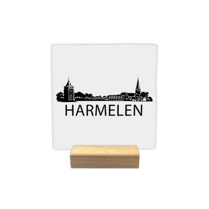 Harmelen skyline - Decoratie tegel - Formaat: - Op deze decoratie tegel staat een zwarte skyline van Harmelen afgebeeld tegen een witte achtergrond. Het silhouet bevat diverse gebouwen, waaronder een opvallende toren en een kerktoren. Onder het silhouet staat in zwarte letters de plaatsnaam Harmelen. Het ontwerp is uitgevoerd in een gedetailleerde zwart-witstijl. - Snelwenskaart