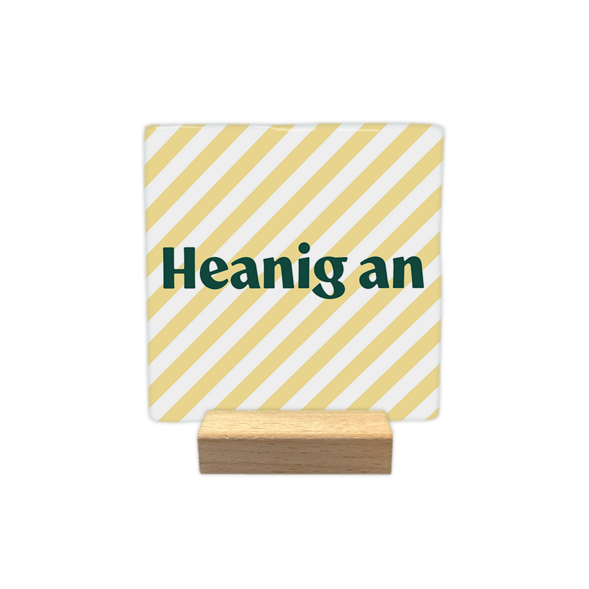 Heanig an - Decoratie tegel - Formaat: - Op deze decoratie tegel staat de tekst "Heanig an" in donkergroene letters centraal in beeld. De achtergrond bestaat uit een patroon van diagonaal lopende, lichtgele en witte strepen. Het ontwerp oogt hierdoor rustig en gestreept. - Snelwenskaart