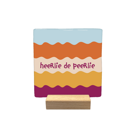 Heerlie de peerlie - Decoratie tegel - Formaat: - Op deze decoratietegel staat de tekst "heeRlie de peeRlie" in donkerpaarse, speelse letters centraal afgebeeld. De achtergrond bestaat uit horizontale, golvende banen in diverse kleuren, waaronder lichtblauw, oranje, beige, geel en donkerpaars. - Snelwenskaart