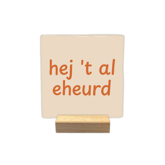 Hej 't al eheurd - Decoratie tegel - Formaat: - Op deze decoratie tegel staat de tekst "hej 't al eheurd" in oranje letters verdeeld over twee regels. Het ontwerp maakt gebruik van een speels lettertype en is geplaatst op een lichtbeige achtergrond. - Snelwenskaart