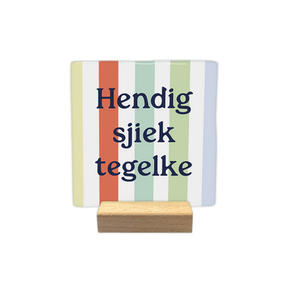 Hendig sjiek tegelke - Decoratie tegel - Formaat: - Op deze decoratie tegel staat de tekst "Hendig sjiek tegelke" in donkerblauwe letters. De achtergrond bestaat uit verticale banen in verschillende pastelkleuren, zoals geel, oranje, groen en blauw. Het ontwerp heeft een kleurrijke en vrolijke uitstraling. - Snelwenskaart