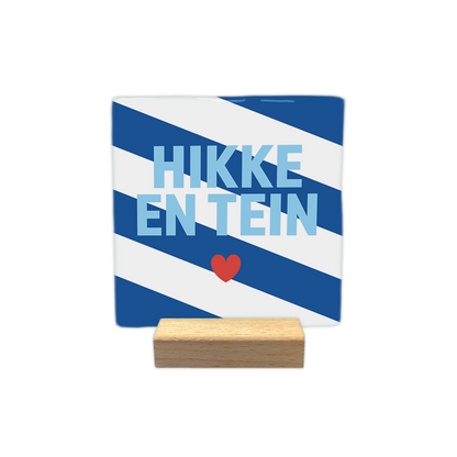 Hikke en tein - Decoratie tegel - Formaat: - Op deze decoratie tegel staat de tekst "HIKKE EN TEIN" in lichtblauwe letters centraal afgebeeld. Onder de tekst is een klein rood hartje geplaatst. De achtergrond van de tegel bestaat uit schuin lopende blauwe en witte banen. - Snelwenskaart