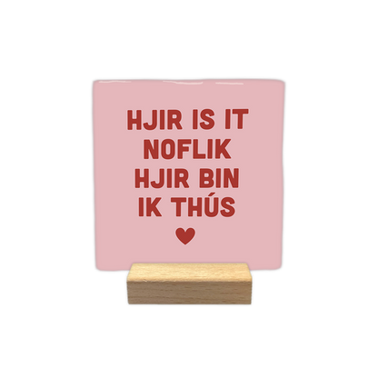 Hjir is it noflik hjir bin ik thús - Decoratie tegel - Formaat: - Op deze decoratie tegel staat de tekst "hjir is it noflik hjir bin ik thús" in rode letters centraal afgebeeld. Onder de tekst is een klein rood hartje geplaatst. De achtergrond van de tegel is lichtroze van kleur. - Snelwenskaart