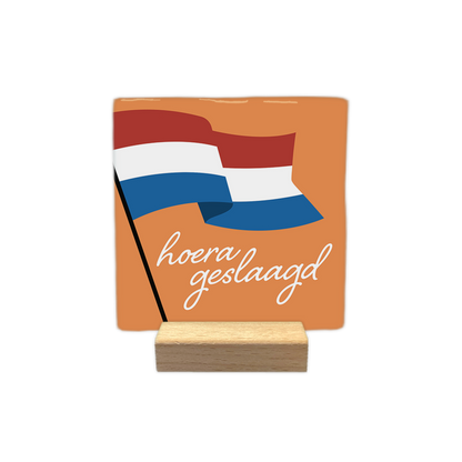 Hoera geslaagd - Decoratie tegel - Formaat: - Op deze decoratie tegel staat de nederlandse vlag. De achtergrond is oranje. Onder de vlag staat in het wit de tekst 'Hoera geslaagd'. - Snelwenskaart