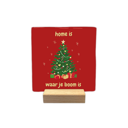 Home is waar je boom is - Decoratie tegel - Formaat: - Op deze decoratie tegel staat een rode achtergrond met een versierde kerstboom in het midden. Onder de boom liggen verschillende cadeautjes en eromheen zijn kleine sterren getekend. Boven en onder de boom staat in gele letters de tekst: home is waar je boom is. - Snelwenskaart