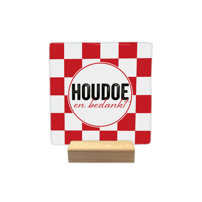 Houdoe en bedankt - Decoratie tegel - Formaat: - Op deze decoratie tegel staat een achtergrond met een rood-wit geblokt patroon. In het midden bevindt zich een witte cirkel met een dunne rode rand. Binnen deze cirkel staat in het groot de tekst "Houdoe" en daaronder in een kleiner cursief lettertype de tekst "en bedankt". Het ontwerp combineert een geometrisch patroon met tekstuele elementen. - Snelwenskaart