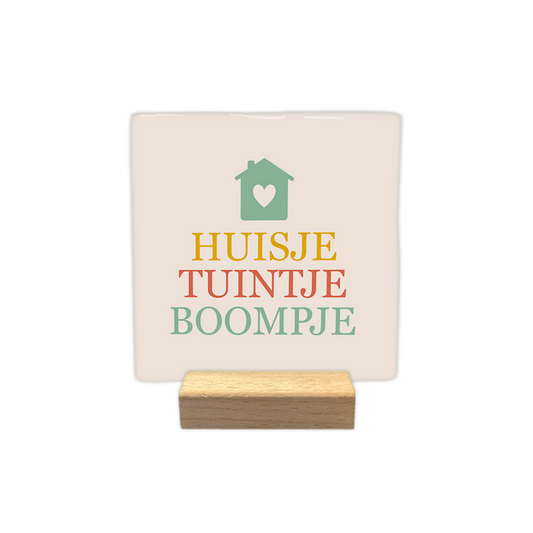 Huisje tuintje boompje - Decoratie tegel - Formaat: - Op deze decoratie tegel staat bovenaan een groen huisje met een wit hartje afgebeeld. Daaronder staat in drie gekleurde regels de tekst "Huisje, tuintje, boompje". Het woord "Huisje" is geel, "tuintje" is oranje en "boompje" is groen gekleurd. De achtergrond van de tegel is lichtbeige. - Snelwenskaart