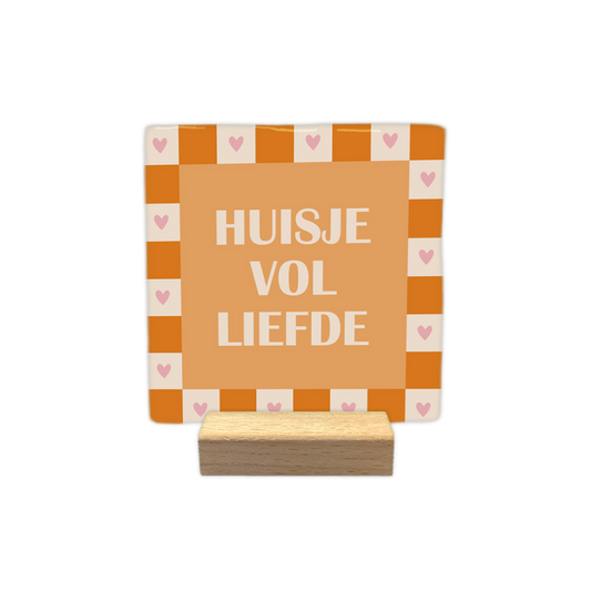 Huisje vol liefde - Decoratie tegel - Formaat: - Op deze decoratie tegel staat centraal de tekst "HUISJE VOL LIEFDE" in witte letters op een oranje achtergrond. De illustratie is omrand door een schaakbordpatroon van afwisselend oranje en lichtbeige vierkanten. In elk van de lichtbeige vierkanten van de rand is een klein roze hartje afgebeeld. - Snelwenskaart