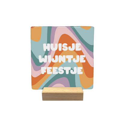 Huisje wijntje feestje - Decoratie tegel - Formaat: - Op deze decoratietegel staat centraal de tekst "HUISJE WIJNTJE FEESTJE" in dikke, witte letters afgebeeld. De achtergrond wordt gevormd door een kleurrijk, golvend patroon in tinten oranje, roze, paars en blauw. - Snelwenskaart