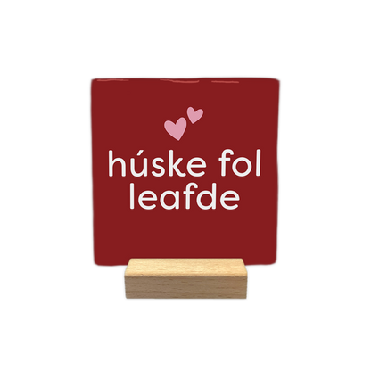 Húske fol leafde - Decoratie tegel - Formaat: - Op deze decoratie tegel staat de tekst "húske fol leafde" in witte letters centraal afgebeeld. Boven de tekst staan twee kleine, lichtroze hartjes. De achtergrond van de tegel is dieprood van kleur. - Snelwenskaart
