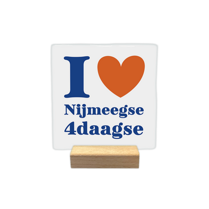 I love Nijmeegse 4daagse - Decoratie tegel - Formaat: - Op deze decoratie tegel staat bovenaan een blauwe hoofdletter "I" naast een oranje hart. Daaronder staat de tekst "Nijmeegse 4daagse" in blauwe letters, verdeeld over twee regels. Het geheel is geplaatst op een witte achtergrond. - Snelwenskaart