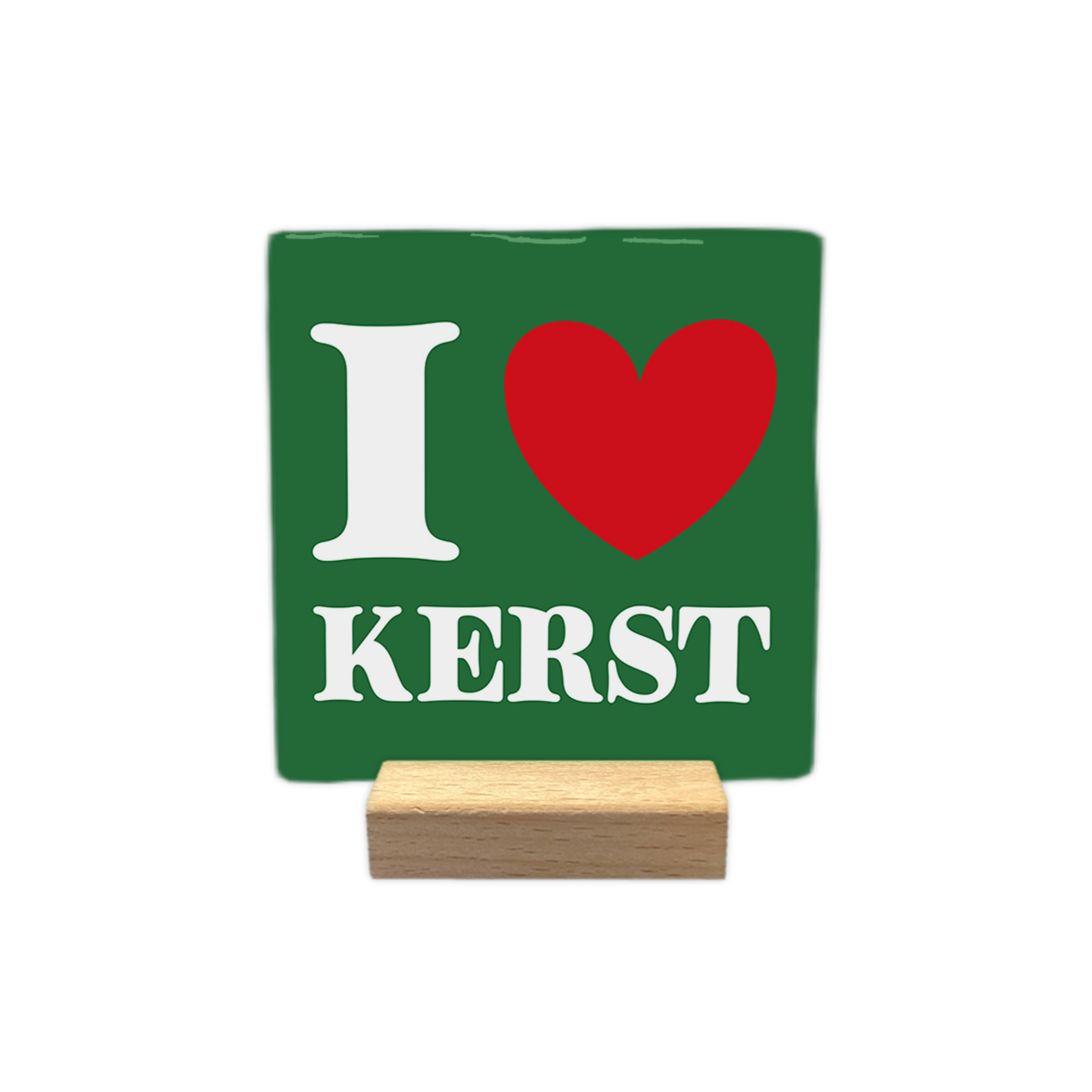 I love kerst - Decoratie tegel - Formaat: - Op deze decoratie tegel staat een groene achtergrond met witte en rode elementen. Links staat een witte letter i en rechts daarvan is een rood hart te zien. Onder dit hart en de letter staat in witte letters het woord kerst. De tegel staat op een kleine houten houder. - Snelwenskaart