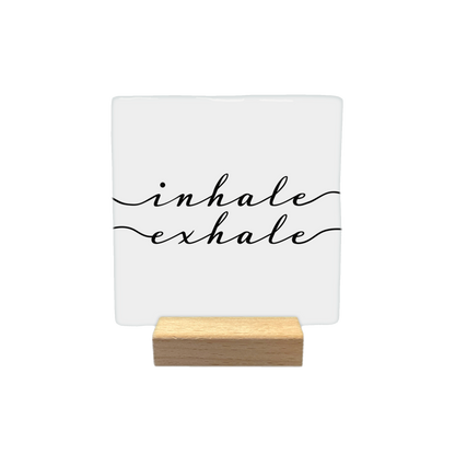 Inhale exhale - Decoratie tegel - Formaat: - Op deze decoratietegel staat de tekst "inhale" en "exhale" in zwarte letters met een elegant, cursief handschrift. Beide woorden worden aan weerszijden geaccentueerd door een golvende lijn die in de tekst overgaat. De tekst is gecentreerd op een witte achtergrond. - Snelwenskaart