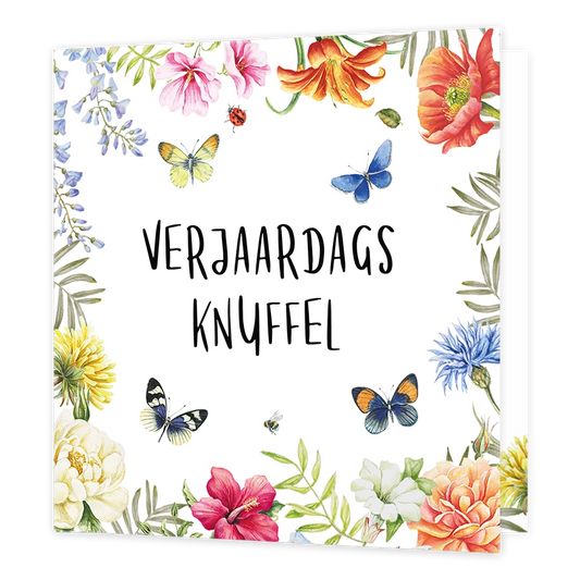 Verjaardagsknuffel - Formaat: Standaard - Vorm: Vierkant - Verjaardagskaart - Op deze wenskaart staat in het midden in zwarte, handgeschreven letters de tekst "VERJAARDAGS KNUFFEL". De tekst wordt omringd door een kleurrijke rand van diverse bloemen, waaronder roze, oranje, gele en blauwe varianten, afgewisseld met groen blad. Tussen de bloemen vliegen verschillende vlinders, een lieveheersbeestje en een bijtje afgebeeld. De illustratie heeft een witte achtergrond en is vormgegeven in een botanische aquare