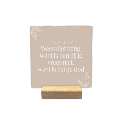 Jesaja 41:10 - Decoratie tegel - Formaat: - Op deze decoratie tegel staat de tekst "Jesaja 41:10" gevolgd door de zin "Wees niet bang, want Ik ben bij je; vrees niet, want Ik ben je God". Deze witte tekst is centraal geplaatst tegen een lichtbruine achtergrond. In de linker- en rechterhoek zijn witte lijntekeningen van bladeren aangebracht. Het gehele ontwerp heeft een rustige en eenvoudige uitstraling. - Snelwenskaart