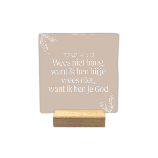 Jesaja 41:10 - Decoratie tegel - Formaat: - Op deze decoratie tegel staat de tekst "Jesaja 41:10" gevolgd door de zin "Wees niet bang, want Ik ben bij je; vrees niet, want Ik ben je God". Deze witte tekst is centraal geplaatst tegen een lichtbruine achtergrond. In de linker- en rechterhoek zijn witte lijntekeningen van bladeren aangebracht. Het gehele ontwerp heeft een rustige en eenvoudige uitstraling. - Snelwenskaart