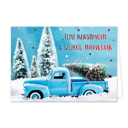 Fijne kerstdagen & gelukkig nieuwjaar - 8 stuks - Formaat: Standaard - Vorm: Liggend - Kerstkaart - Op deze wenskaart staat een sfeervolle afbeelding van een lichtblauwe oldtimer pick-up truck die door een dik pak sneeuw rijdt. In de laadbak van de truck ligt een besneeuwde kerstboom, vastgebonden met een rood-wit gestreept touw. De achtergrond toont een winters landschap met wazige, besneeuwde dennenbomen onder een helderblauwe lucht die versierd is met kleine rode en witte sterretjes. Rechtsboven staat d