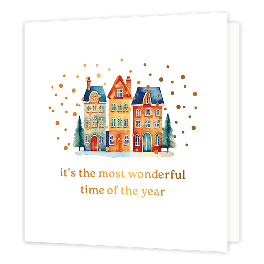 It's the most wonderful time of the year - Formaat: Normaal - Vorm: Vierkant - Kerstkaart - Op deze wenskaart staat een sfeervolle aquarel-illustratie van drie kleurrijke, karakteristieke grachtenpanden in winterse sferen. De huisjes, in tinten blauw, geel en oranje, staan in de sneeuw en worden geflankeerd door twee groene dennenboompjes. Het tafereel wordt omringd door een feestelijke regen van goudkleurige stipjes tegen een helderwitte achtergrond. Onderaan de kaart staat in elegante gouden letters de t