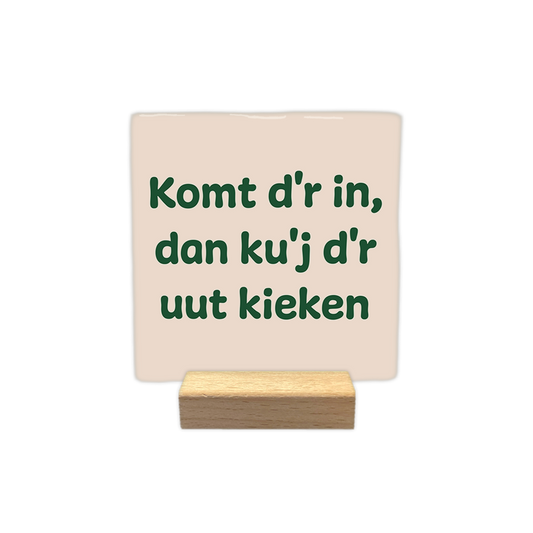 Komt d'r in, dan ku'j d'r uut kieken - Decoratie tegel - Formaat: - Op deze decoratie tegel staat de tekst "Komt d'r in, dan ku'j d'r uut kieken" verdeeld over drie regels. De letters zijn donkergroen en in een speels lettertype weergegeven. De achtergrond heeft een lichtbeige kleur. - Snelwenskaart